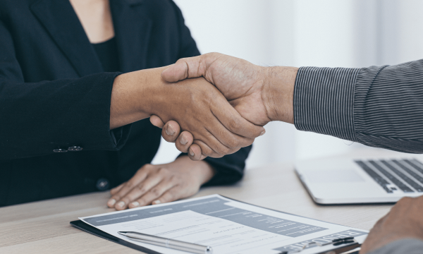Two people shaking hands at a table with a clipboard
