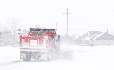 A red snow plow clearing the roads during a winter storm